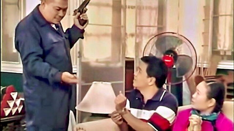 Armed man in blue jacket points gun at terrified couple on couch