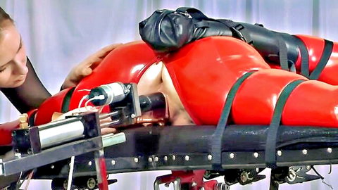 Blonde in red latex restrained on back for fucking machine penetration in BDSM