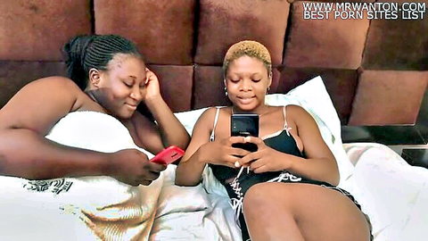 Two ebony lesbian roommates cuddling in bed, checking phones seductively