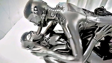 Two latex-clad women in intense BDSM strapon embrace, shiny fetish outfits