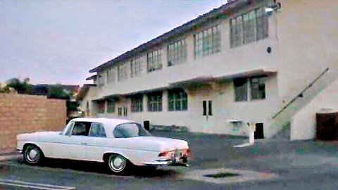 Vintage scene from Taboo IV (1985): White Mercedes car parked outside beige building