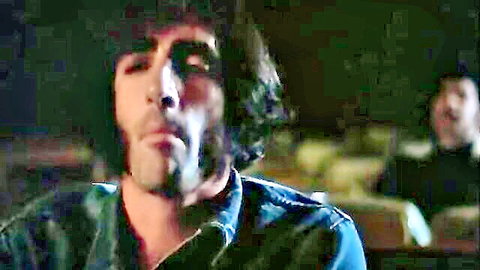 Rugged curly-haired man in denim jacket stares intensely in 1977 grindhouse scene