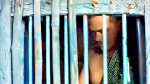 Shirtless Indian man in prison cell, gazing through bars in erotic Telugu scene