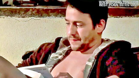Sexy man in open camo robe exposing bare chest reads book beside woman's bare thigh tease