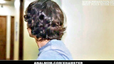 Curly-haired MILF in gray shirt, side profile in hallway, teasing anal fun