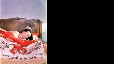 Brunette woman lying nude in bed, exposing breasts with teasing smile