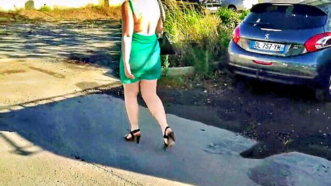 Woman in sheer green transparent dress walking outdoors in high heels, exhibition style