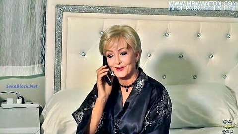 Seductive blonde MILF in black silk robe talking on phone smiling on luxurious bed