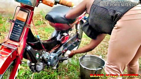 African woman bends over washing red motorcycle, tight pants highlight curves
