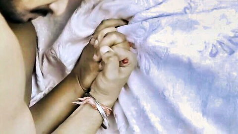 Intimate couple holding hands under white sheets in bed, suggesting post-sex closeness