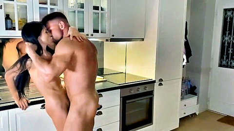 Muscular naked man passionately kissing nude brunette woman in steamy kitchen embrace