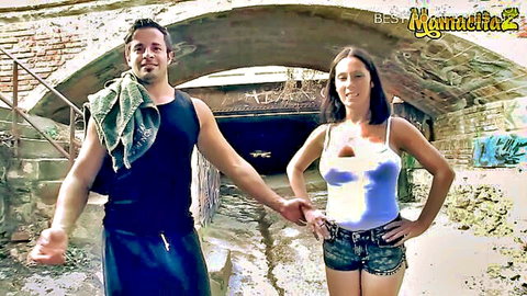 Sexy Latina brunette in tight tank top and daisy duke shorts holds hands with muscular hunk outdoors