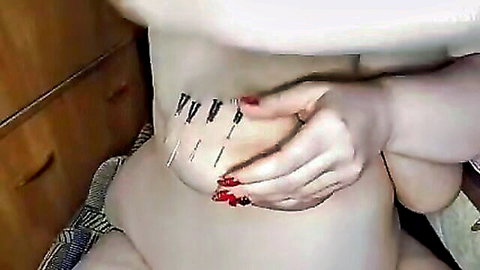 Pale woman with needles piercing skin near big tits in solo fetish play