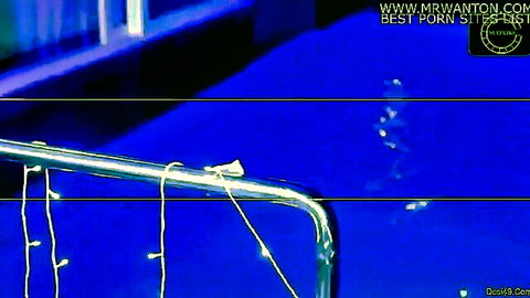 Blurry nighttime pool with silver railing, string lights, splashing water and indistinct figures.