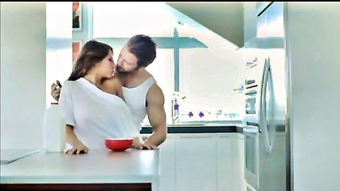 Intimate couple kissing in kitchen, brunette in slipped white top, muscular guy shirtless