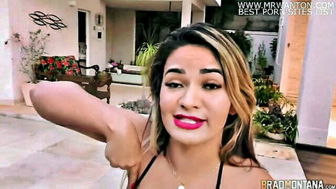 Tanned Latina in red bikini posing arm up outdoors