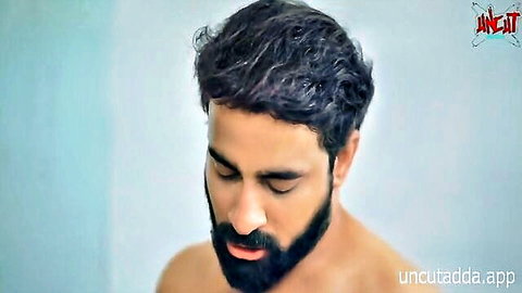 Bearded Indian man with curly hair looking down shirtless exposing bare chest in closeup