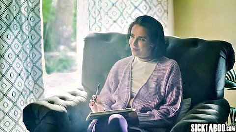 Brunette beauty in purple cardigan sits pensively writing in notebook by sunny window