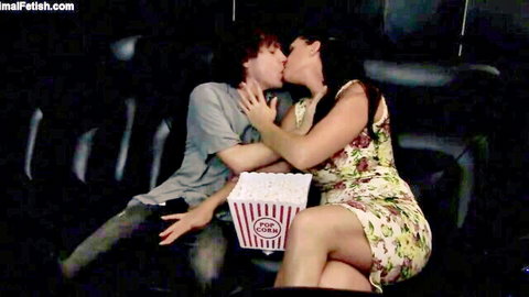 Curvy brunette passionately kissing guy in movie theater seats holding popcorn