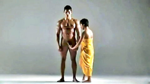 Muscular nude Thai man holds hands with petite brunette in yellow towel