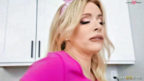 Blonde MILF housewife in tight pink top smirks naughtily in kitchen