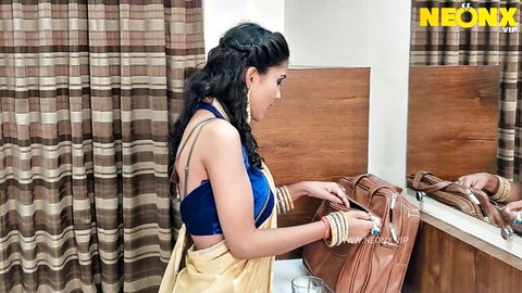 Young skinny Indian brunette in yellow saree and blue blouse handling bag at bedroom mirror