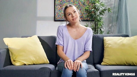 Naomi Swann in seductive purple top, sitting thoughtfully on couch