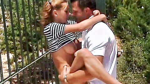Blonde babe with exposed tits and spread shaved pussy held up by stud against outdoor fence