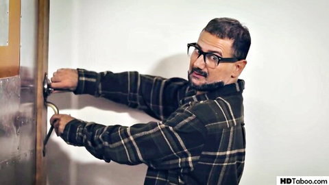 Bearded man in glasses and plaid shirt grips doorknob tightly in taboo scene