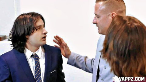 Two suited men gesturing and talking closely with long-haired brunette woman in formal setting