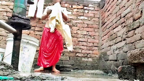 Sexy Indian woman covering tits with white towel in wet red skirt at outdoor water pump