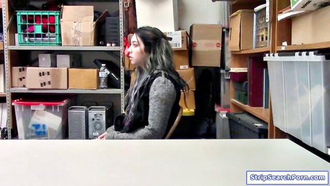 Skinny teen with small tits and long hair sits clothed in gray sweater in cluttered storage room