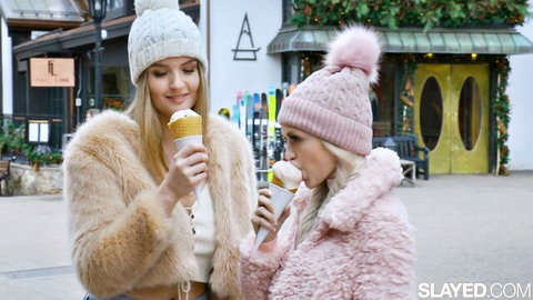 Two sexy young blondes in fur coats licking vanilla ice cream cones teasingly outdoors