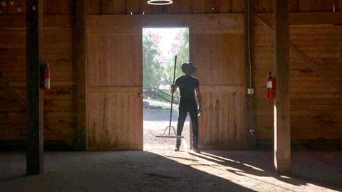 Isiah Maxwell as cowboy in barn holding pitchfork, teasing farm scene with Arabelle Raphael