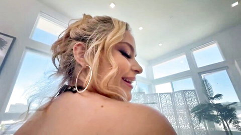 Nicole Aria smiling profile in black top, blonde hair and hoop earrings