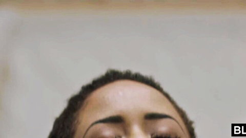 Sensual close-up of curly-haired black babe gazing up with sultry eyes ready to suck cock