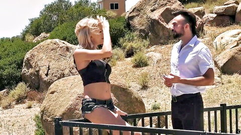 Blonde babe with big tits in skimpy crop top and tiny shorts teases beside spiky-haired guy on rocky fence outdoors