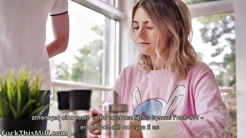 Skinny blonde in pink bunny hoodie holds mug while guy stands behind her in kitchen