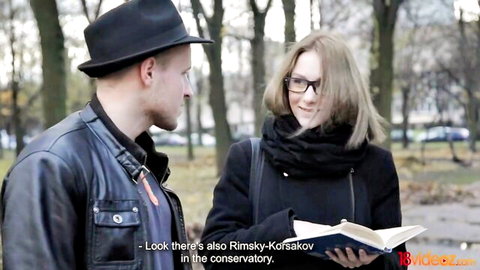 Nerdy blonde with glasses holds Rimsky-Korsakov book, tempted by young man outdoors
