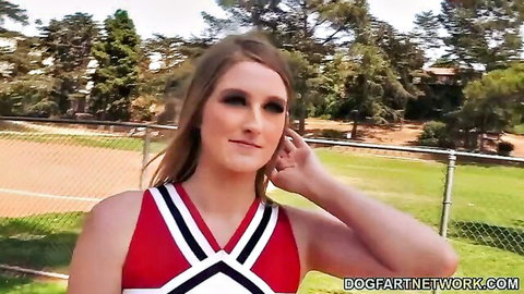 Blonde cheerleader posing seductively outdoors in tight red uniform showing cleavage