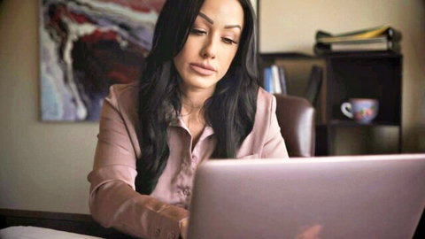 Sexy brunette MILF babe in pink blouse typing on laptop at office desk solo tease