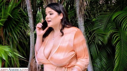 Dani Valentina in low-cut orange dress showing huge cleavage, curvy Latina on phone