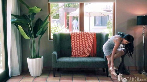 Sexy Asian woman in short gray dress squats bending over green couch putting on high heel
