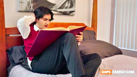 Handsome young man in red vest and white shirt reading large book on bed