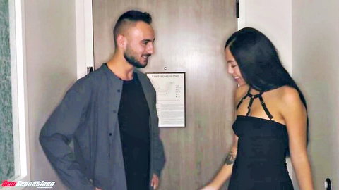Latina brunette in sexy black harness dress flirts smiling with husband in hotel doorway