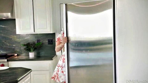 Curvy blonde MILF peeking teasingly from behind open fridge door in floral dress kitchen