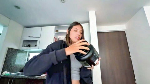 Fit babe in gray tank top holds thick black shaker to lips drinking in kitchen