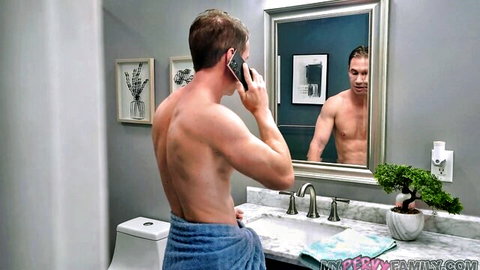 Muscular shirtless hunk in low towel talks on phone admiring ripped reflection in bathroom mirror