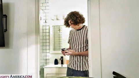 Curly-haired guy in striped shirt holds phone in bathroom door from Mona Azar's My Dad's Hot Girlfriend