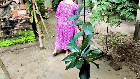 Desi aunty in flowing purple dress walks in lush yard, teasing outdoor cleanup tease
